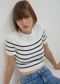 Weißes, gestricktes Crop-Top mit schwarzen horizontalen Streifen, rundem Ausschnitt und kurzen Ärmeln, kombiniert mit hellblauen, hoch taillierten Jeans.