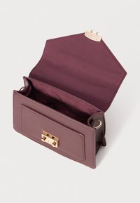 Sac à main en cuir bordeaux avec un fermoir doré, ouvert, révélant un intérieur en tissu lisse. Il possède une poche avant plate et des coins arrondis.