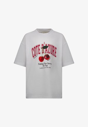 Witte oversized T-shirt met rode tekst 'COTE D'AZURE' en een ontwerp van kersen met een groen blaadje. Korte mouwen, ronde hals.