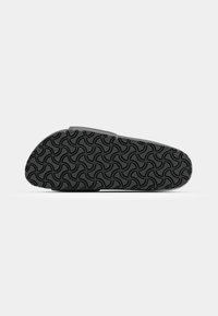 Semelle d'une chaussure noire avec un motif géométrique incurvé, présentée à plat sur fond blanc.