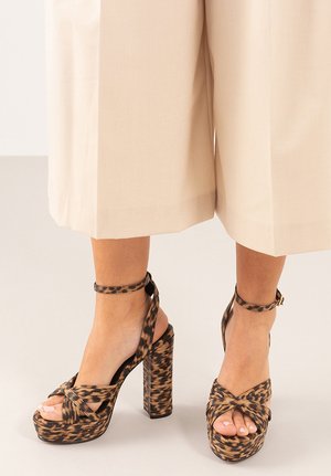 Sandalias de tacón alto con estampado de leopardo, plataforma gruesa, tira en el tobillo y diseño trenzado en la parte delantera. El material parece texturizado y duradero.