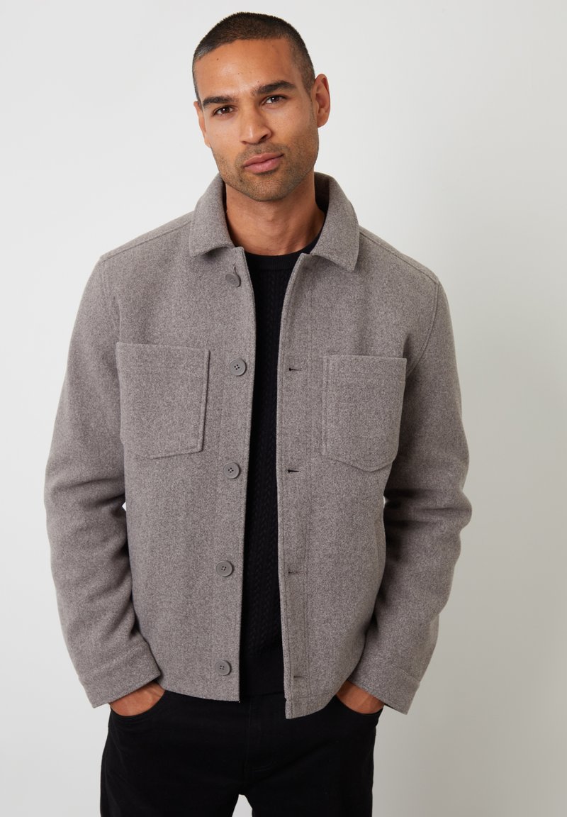Szara kurtka z wełny z zapięciem na guziki, dwoma przednimi kieszeniami, kołnierzykiem oraz teksturowaną podszewką, noszona na ciemnym swetrze.