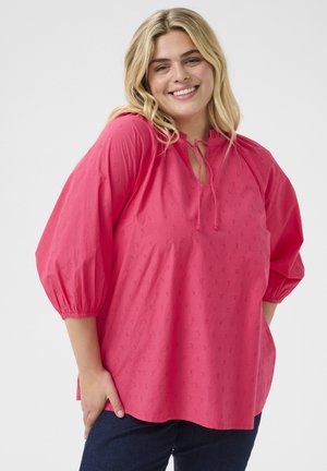 Roze, losse blouse met een ronde hals, korte ballonmouwen en een strikdetail. Heeft een geweven patroon over het geheel.