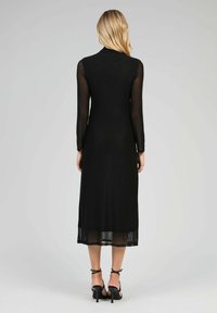 Robe noire mi-longue avec de longues manches transparentes et une silhouette ajustée. Texture lisse, design subtil et un col simple.