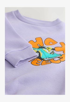 Lillat värvi dressipluus soonikkoes mansettide ja kaelusega. Kaunistatud värvika auto graafikuga, millel on oranži ja musta värviga tekst "Hot Wheels".