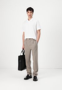 Vit polo shirt, beige veckade byxor, svarta läderskor och en svart tote-väsk. Släta ytor, minimalistisk design och neutrala färger.