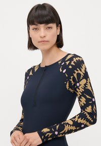 Marine langermet våtdrakt med glidelås på fronten. Ermet har et gull- og rosa abstrakt mønster. Glatt, fleksibelt materiale designet for komfort.