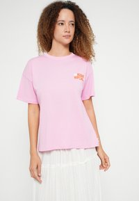 Tricou din bumbac roz deschis, cu mâneci scurte, având inscripția „Aloha Rip Curl” în portocaliu pe piept. Croiala lejeră și textura moale.