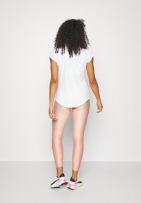 Top atletico bianco a maniche corte abbinato a leggins rosa con sfumature e strisce ondulate. Scarpe sportive con dettagli neri e verde neon.