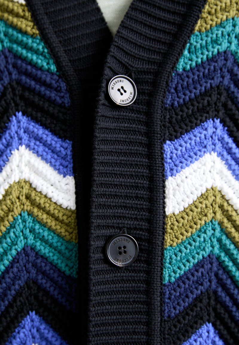 Cardigan all'uncinetto con motivo a zig-zag nei colori nero, verde, viola, blu e bianco, con texture a costine e due bottoni neri.