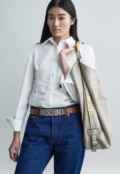 Beige kézi táska arany kiegészítőkkel, fehér gombos inggel és sötétkék farmerral, amelyhez barna Moschino öv tartozik.