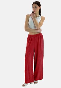 Rode, losse, structuurpant met een elastische tailleband; gecombineerd met een aansluitende, mouwloze witte top en open teen hakken.