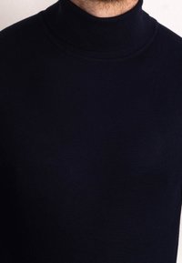 Granatowy golf wykonany z gładkiej, dzianinowej tkaniny z prążkowanym kołnierzem, o dopasowanym kroju i minimalnej liczbie szwów.