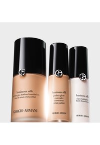 Tres productos Luminous Silk de Giorgio Armani: una base de maquillaje, un corrector y un iluminador. Botellas de cristal con elegantes tapas negras y acentos de logotipo plateado.