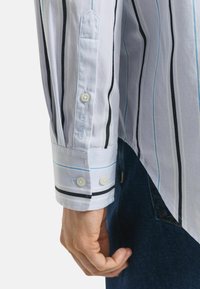 White long-sleeve shirt with vertical black and blue stripes, buttoned cuff, and embroidered logo on the sleeve, made of a smooth fabric.
