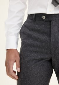 Szare wełniane spodnie cechują się gładkim przodem, bocznymi kieszeniami oraz zapięciem na guzik. Połączone z białą koszulą i wzorzystym krawatem.