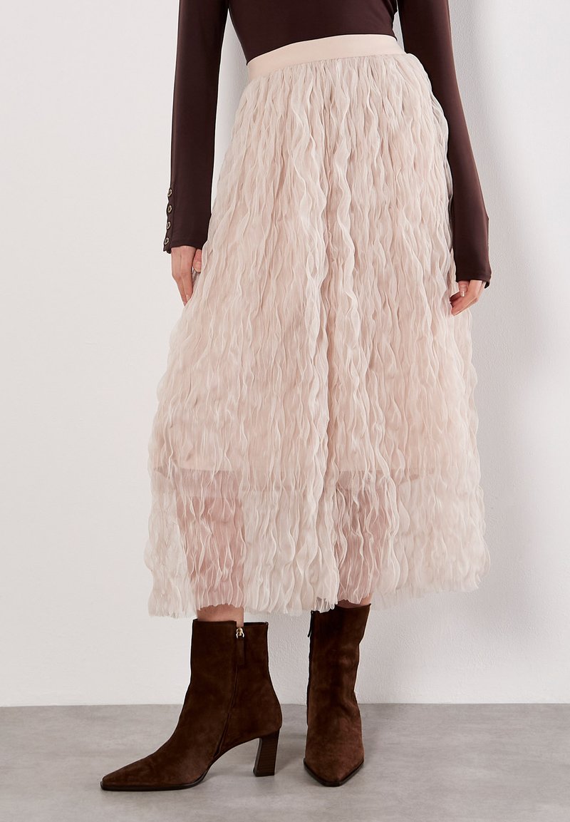 Jupe midi tiered rose pâle avec un design texturé ondulé. Tissu doux et taille ajustée. Associée à des bottines en suède marron.