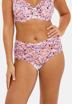 Vrouw draagt hoge taille bloemenkant lingerie met multicolor roze, paars en rood patroon op witte achtergrond, hand op heup.