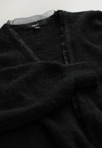 Cardigan noir en tissu doux et texturé avec une bordure noire transparente le long de l'encolure, dotée de poignets côtelés et d'une coupe décontractée.