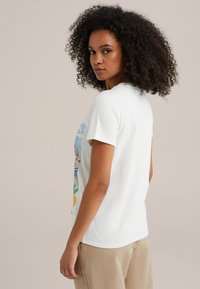 Witte katoenen t-shirt met een grafische print van kleurrijke huizen en fruit. Korte mouwen, ronde halslijn, ontspannen pasvorm.