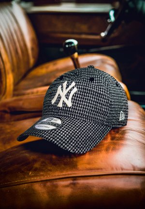 Black and white houndstooth New York Yankees cap resting on a brown leather car seat with vintage gear shift visible.