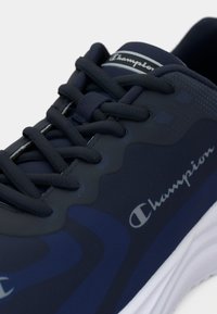 Tamno plava sportska cipela s teksturiranim gornjim dijelom i glatkim akcentima. Sadrži klasičan dizajn vezivanja i "Champion" logotip sa strane.