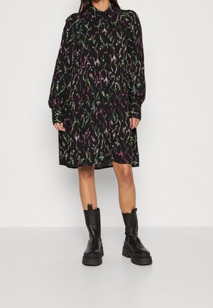 Abito nero con colletto, maniche lunghe e silhouette fluida. Presenta motivi astratti colorati in verde, viola e rosa. Abbinato a stivaletti neri chunky.