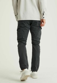Cargo kalhoty v tmavě šedé tkanině se slim fit střihem, s bočními kapsami a elastickými manžetami. Kombinováno s bílými teniskami pro kontrast.