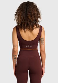 Bordeauxrød atletisk crop top med rundet ryg og logo på båndet, kombineret med højtaljede leggings med sidelommer.