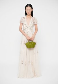 Λευκό φόρεμα με κεντήματα λουλουδιών, διάφανα κοντά μανίκια και βαθύ V-λαιμόκοψη, συνδυασμένο με μια μικρή πράσινη τσάντα με κοντά χερούλια.