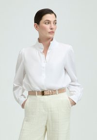 White collared blouse with button-down front and puffed sleeves, paired with light beige belted pants featuring a textured pattern.