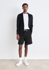 Navy blazer, white t-shirt, and black shorts; white sneakers; natural fiber texture; tailored design with pockets; casual yet structured look.