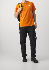 Oranžové bavlněné tričko s malým logem, spárované s černými cargo kalhotami s několika kapsami a černými robustními botami.