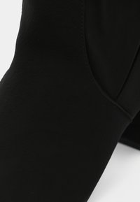 Μαύρο μποτάκι αστραγάλου από λείο υλικό, με κομψό σχέδιο, ψηλή κοπή και ελάχιστες ραφές.