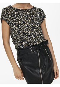 Femme portant un haut à manches courtes à motifs noir, blanc et beige, rentré dans une jupe en cuir noir taille haute avec des détails de fermeture éclair et de ceinture.