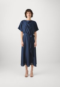 Robe midi bleu marine fluide avec un décolleté drapé, des manches courtes et une ceinture à la taille. Tissu lisse et léger avec un ourlet en couches.