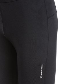 Sort strækbare leggings med en glat tekstur, som har en syet søm og et hvidt "NORTH BEND" logo nederst til venstre.