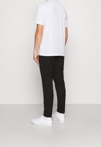 Bílý krátký rukáv tričko, černé slim-fit kalhoty a bílé tenisky, viděné zezadu na jednobarevném pozadí.