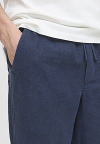 Tmavě modré kalhoty s texturovanou látkou, elastickým pasem a bočními kapsami; kombinované s bílým, lehce volným tričkem.