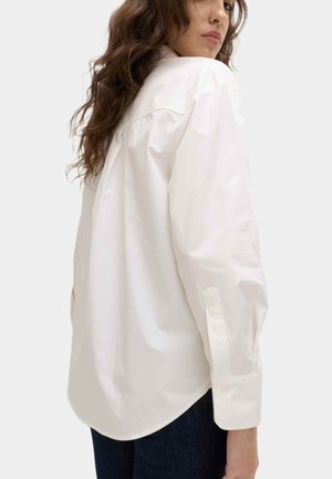 Hvid skjorte med knapper, lavet af bomuld med en glat tekstur, med en buet kant og lange ærmer med knapmanchetter.