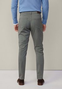 Grijze slim-fit chino's met achterzakken en een leren label. Het materiaal is soepel met een subtiele textuur. Gecombineerd met donkerbruine schoenen.