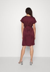 Bordeaux jurk met korte mouwen, elastische taille en een gladde textuur, gecombineerd met schoenen met blokhak en een patroon.
