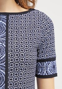 Kortärmad topp med en blandning av blå och svarta mönster, med en texturerad design, solid svart kant och rund halsringning.