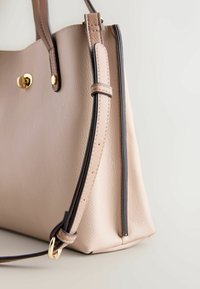 Sac à main en cuir beige avec ferrures dorées, surpiqûres contrastantes et design structuré. Comprend une bandoulière détachable et un bord latéral.