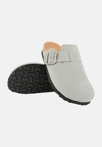 Gray suede clogs with a metallic buckle, featuring a smooth upper and textured black rubber sole, showcasing a casual design.