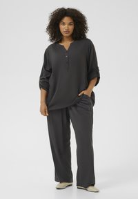 Volný šedý dvoudílný outfit s tričkem ve stylu henley, které má knoflíky a ohrnuté rukávy, doplněný o odpovídající kalhoty rovného střihu.