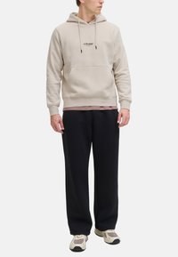 Beige hoodie med frontlomme og logo, lagd over en pink skjorte. Sammen med løse sorte bukser og lyse sneakers.
