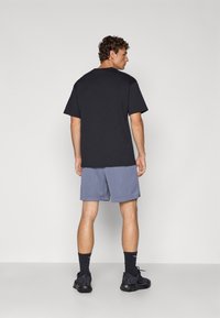 Camiseta de algodón negra, pantalones cortos de malla morados, zapatillas deportivas negras y calcetines negros. Diseño sencillo, corte relajado y tejido transpirable.