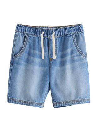 Dreng, der balancerer på ét ben iført en t-shirt med hajmotiv, denimshorts, blå sneakers og en blå bøllehat med hajtryk.