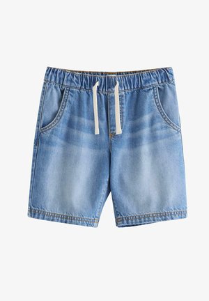 Chłopiec balansujący na jednej nodze, ubrany w koszulkę z motywem rekina, jeansowe szorty, niebieskie trampki i niebieski kapelusz typu bucket z nadrukiem rekina.